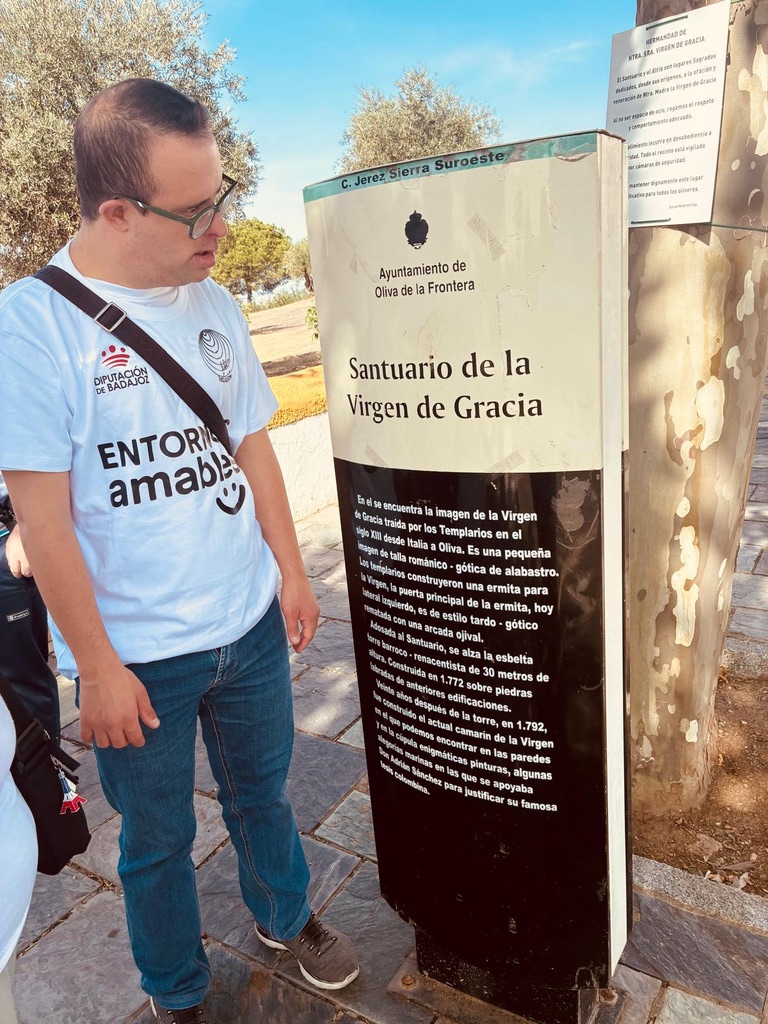 Participante de Entornos Amables junto al panel informativo del Santuario de la Virgen de Gracia, en Oliva de la Frontera