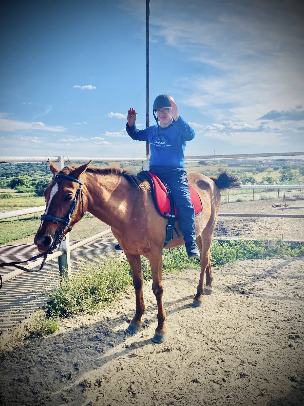 Un participante sonríe y levanta los brazos durante una actividad de equitación adaptada al aire libre